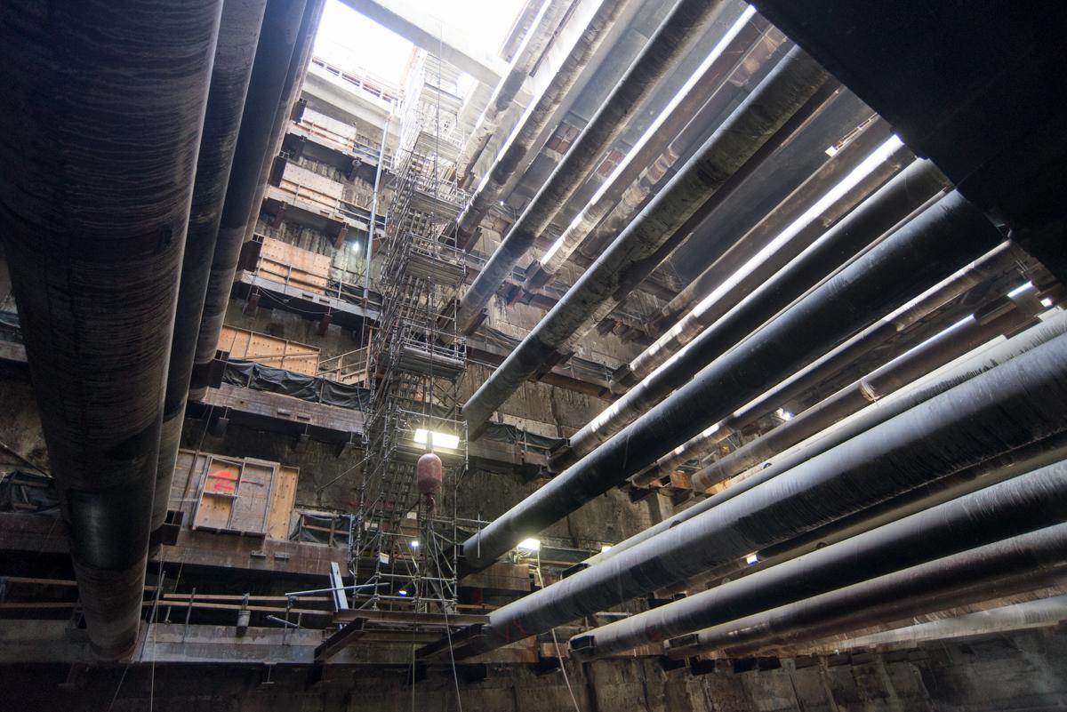 Large industrial pipes and steel support structures inside underground transit station construction cavity.
