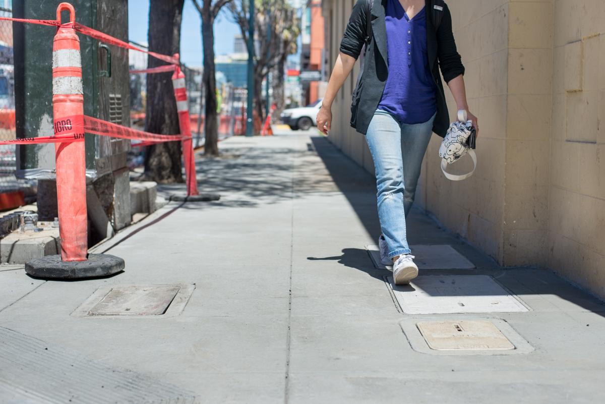 Woman walking on restored sidewalk section on 4th Street with construction barriers visible.