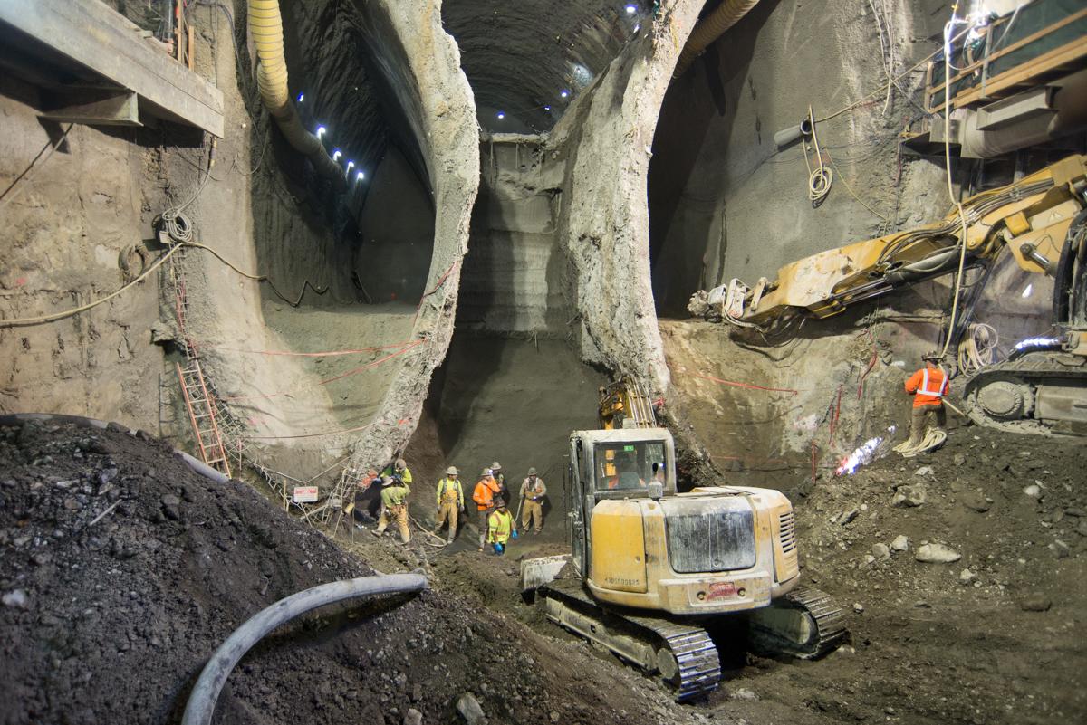 Workers and excavator in underground tunnel cavern during station construction and excavation.