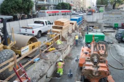 Construction work at Union Square Garage with excavation equipment, workers, and shoring walls on Geary Street.
