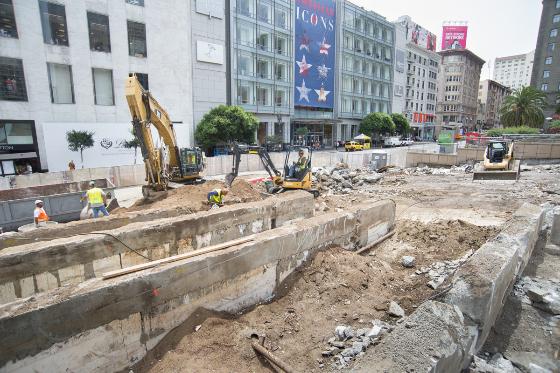 Construction site with excavators removing concrete debris on urban street surrounded by buildings