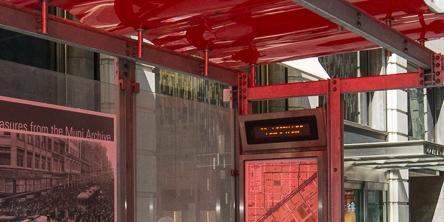 Red transit shelter with digital display sign showing route information.