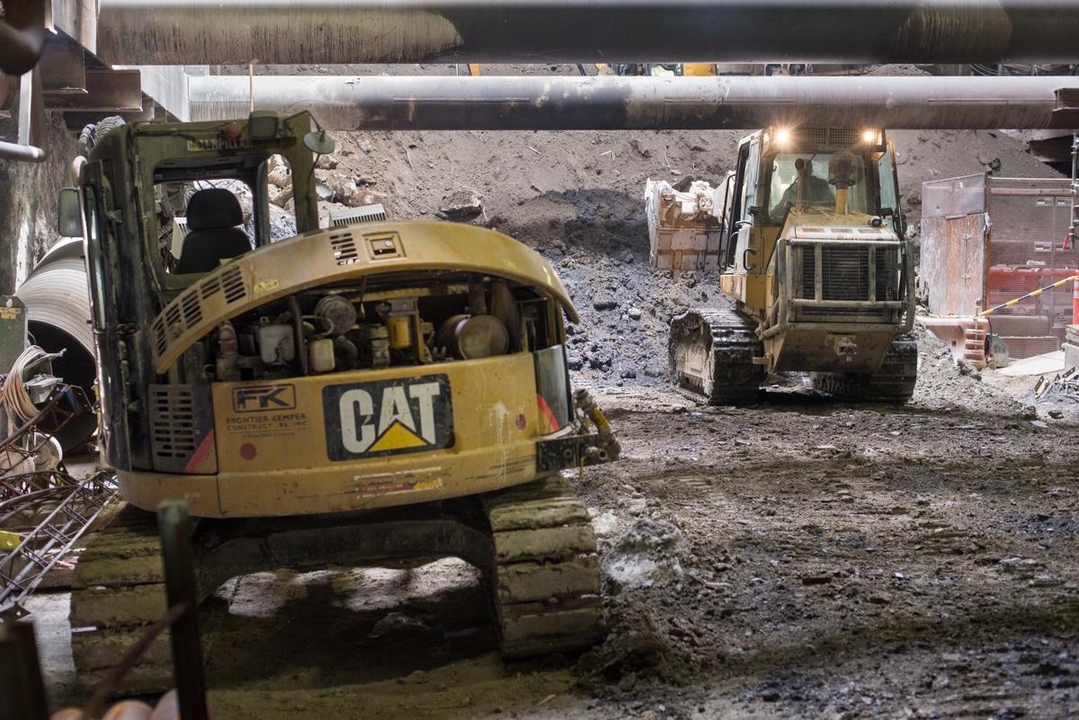 CAT excavator and bulldozer operating at underground transit construction site with exposed rock and soil.