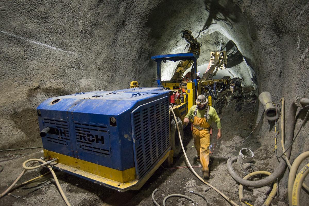Workers operate drilling equipment in underground tunnel during Central Subway construction.
