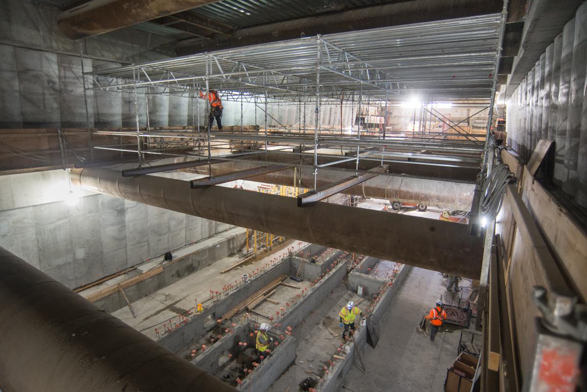 Construction workers in safety gear on scaffolding above an underground transit platform during renovation work.