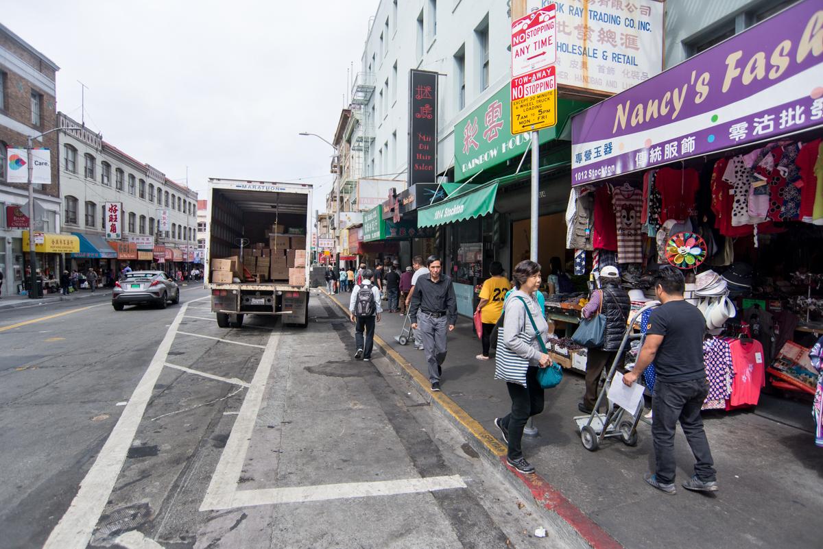 Busy Stockton Street in San Francisco's Chinatown with pedestrians, storefronts, and a delivery truck.