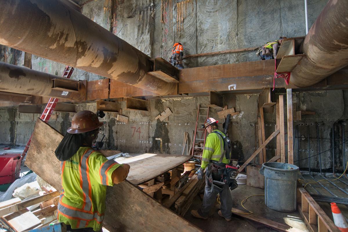 Workers in safety gear construct concrete forms inside a transit station headhouse during repair work.