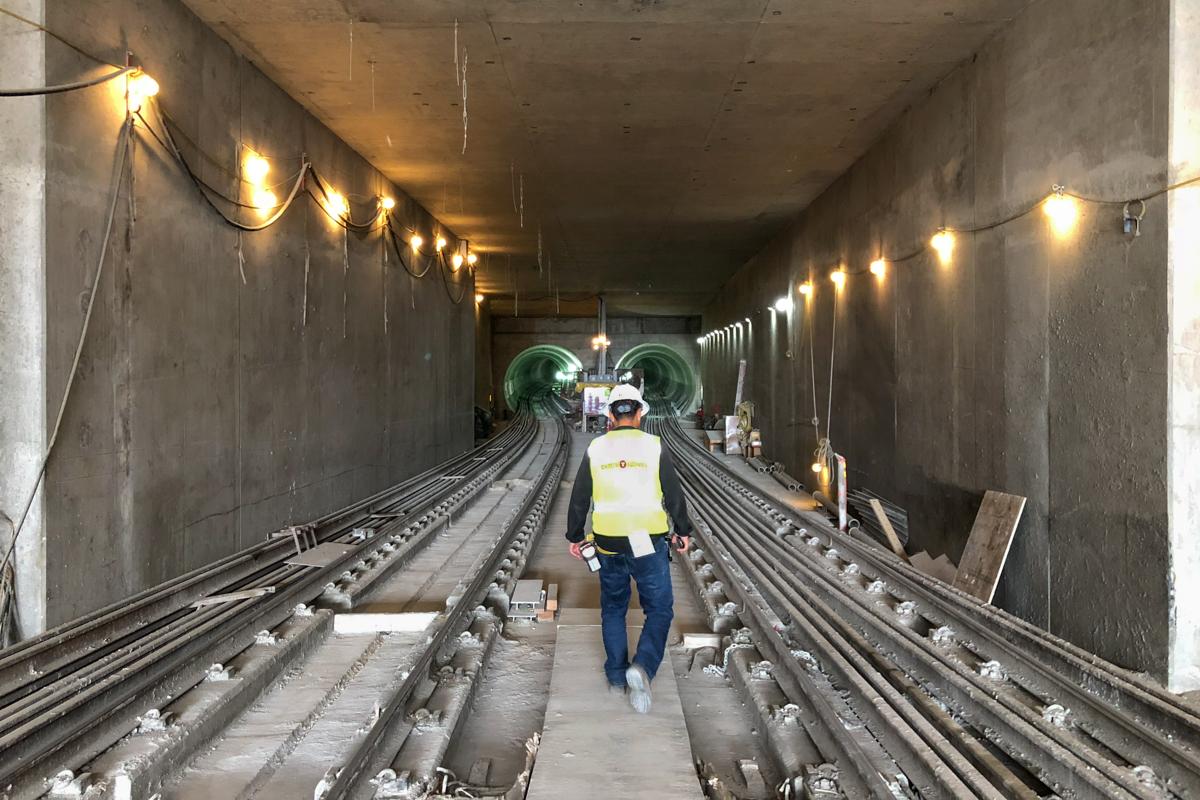 Worker in safety gear walking through underground transit tunnel with dual tracks and overhead lighting.