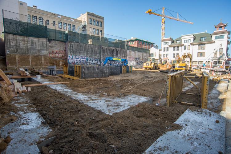 Construction site with shallow perimeter walls, heavy equipment, and crane at Chinatown Station property.
