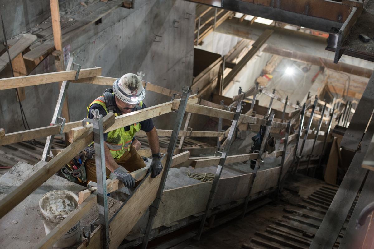 Construction worker in safety gear installing plywood on staircase framework inside Union Square/Market Street Station.