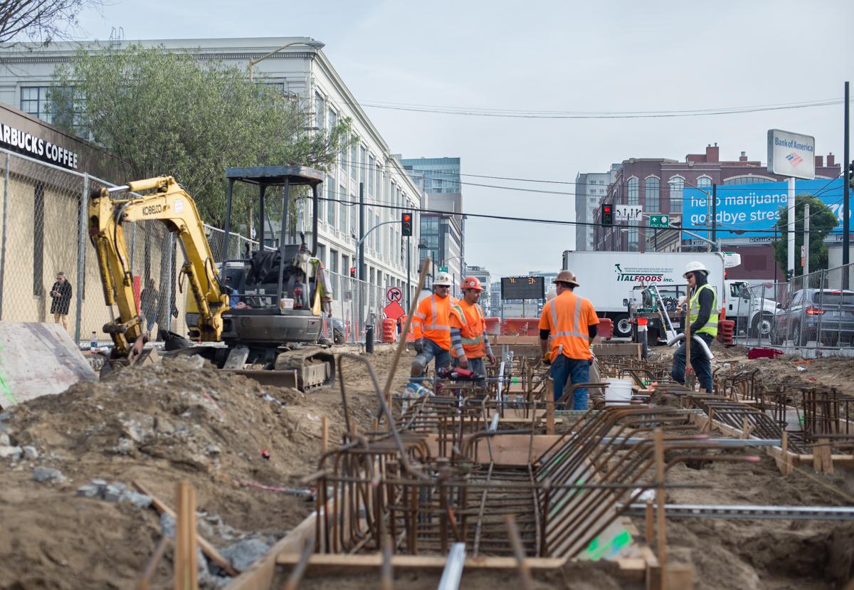Construction crew in orange vests installing underground utilities at 4th and Brannan, with excavator and equipment visible on urban street.