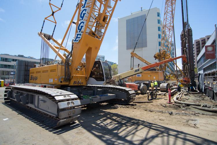 Construction crew works on underground wall installation at Yerba Buena/Moscone Station site with heavy equipment and cranes.