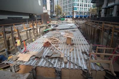 Construction site with corrugated steel panels and reinforcing beams being installed for transit station roof.