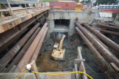 Underground station box construction with concrete structure and large pipes in excavated trench.