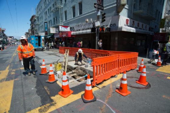 Construction work on Stockton Street with orange barriers, cones, and worker in safety vest.