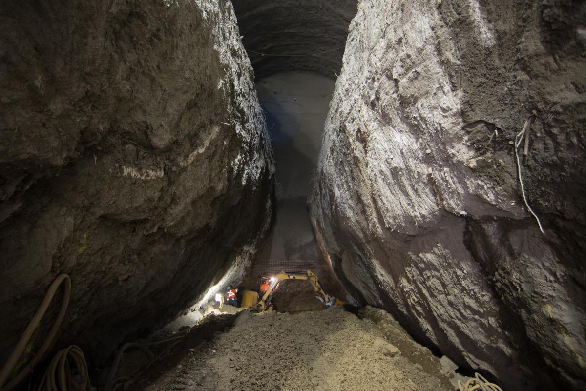 Workers and equipment inside underground tunnel excavation between concrete walls.