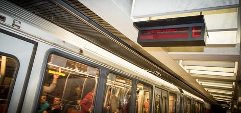 Subway train at platform with overhead digital display sign above.
