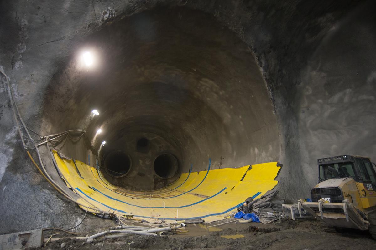 Large tunnel interior with yellow protective covering, construction equipment, and LED work lights illuminating the concrete walls.