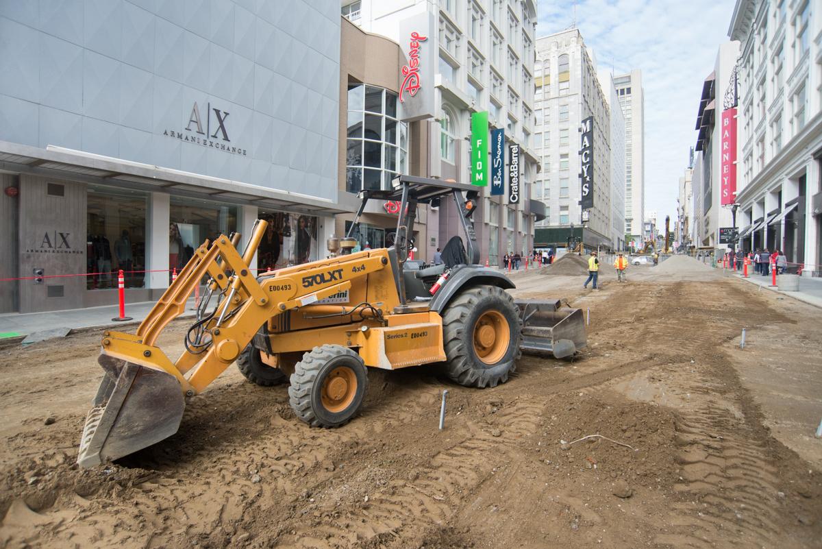 Yellow construction equipment grades dirt on Stockton Street in downtown San Francisco during Central Subway construction.