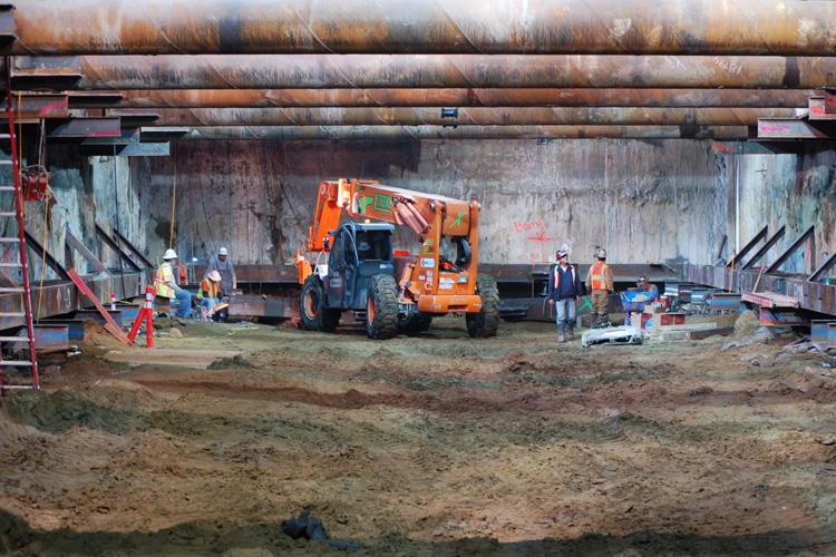 Construction crew operating orange machinery inside underground tunnel launch box on 4th Street.