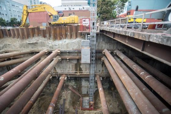 Construction site with large pipes, excavation equipment, and yellow machinery at underground transit station.