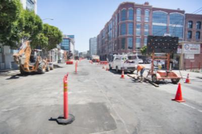 Construction crew working on street with red traffic cones and equipment at urban intersection.