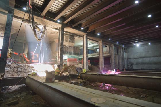 Underground transit tunnel under construction with temporary steel reinforcing and access shaft lighting visible.