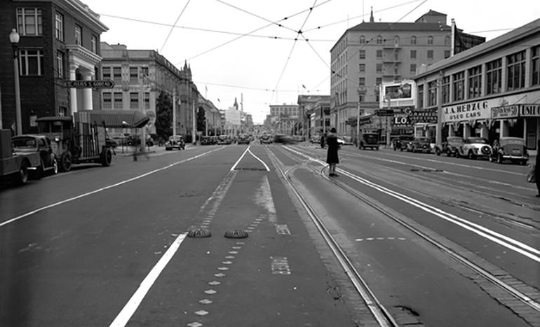 Historic Van Ness Avenue with streetcar tracks, early 20th century buildings, and vintage automobiles.