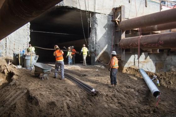 Construction workers in safety vests coordinate rebar installation at an underground transit project site.