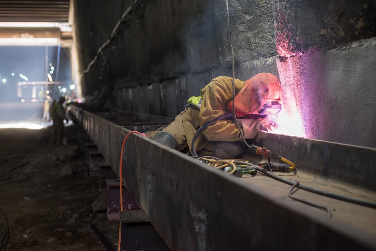 Worker welding steel reinforcement inside Union Square station box during construction.