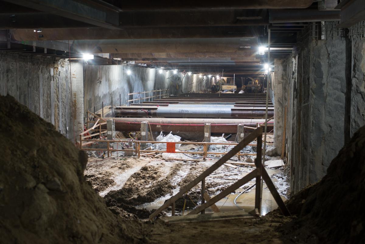 Underground transit station excavation with temporary steel bracing and support structures under construction lighting.