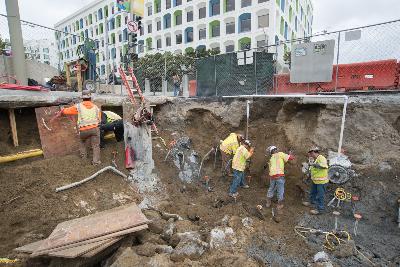 Construction workers excavate deep pit for Yerba Buena Moscone Station near downtown buildings.