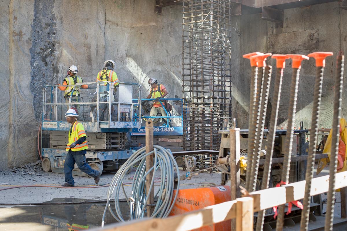 Construction workers on elevated platform removing concrete from station headhouse exterior walls.