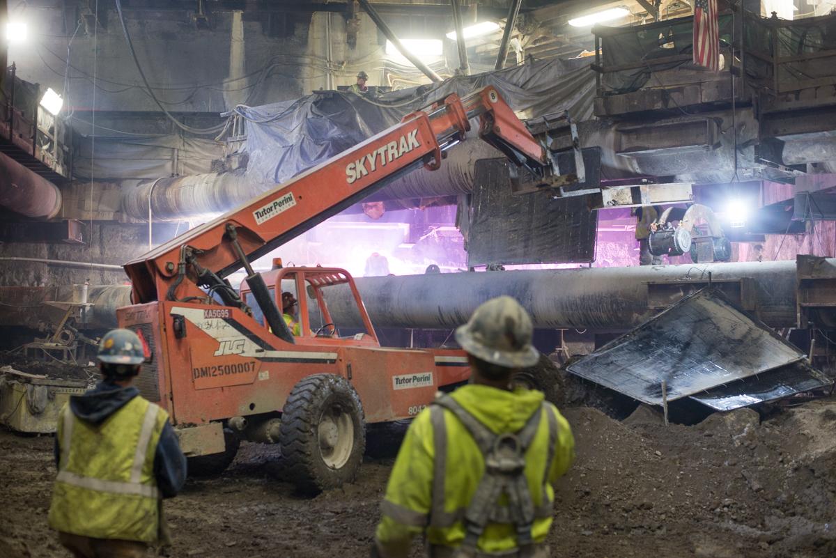 Workers in safety vests operate a Skytrak lift inside an underground construction site for the Central Subway project.