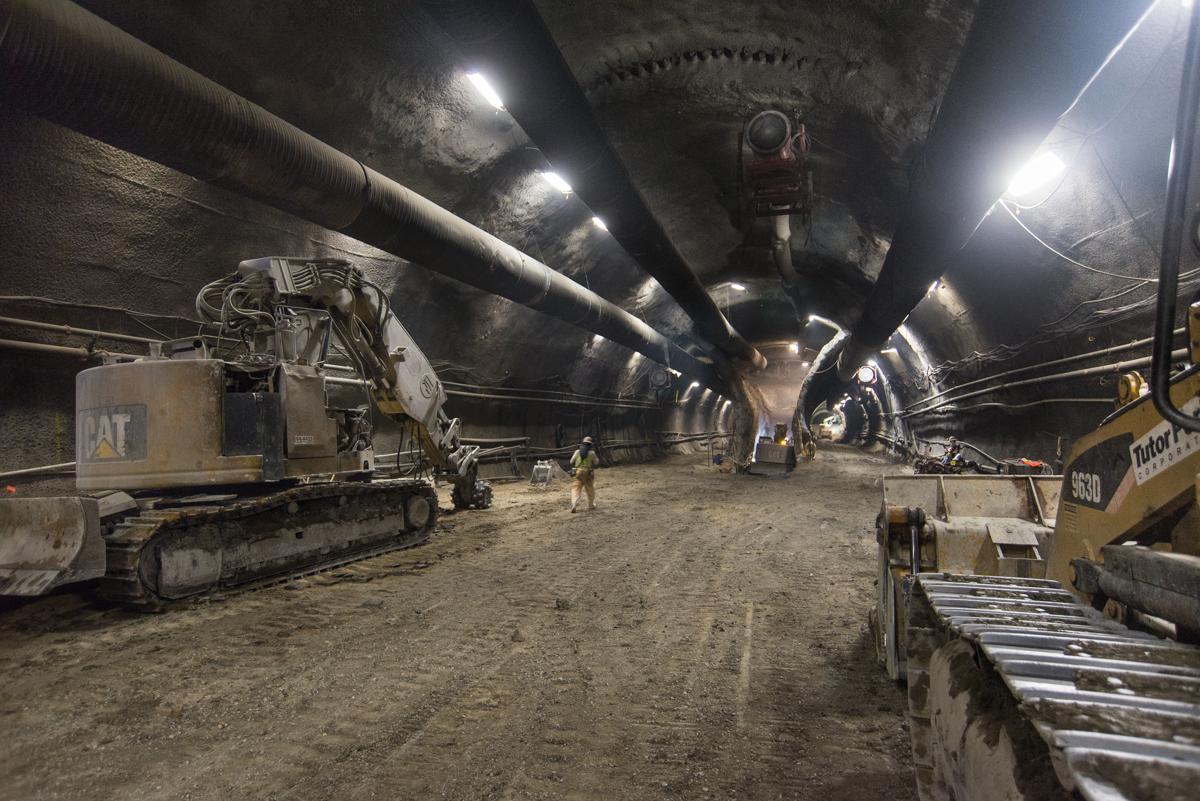 Underground tunnel construction site with excavators and heavy equipment working on platform cavern excavation.