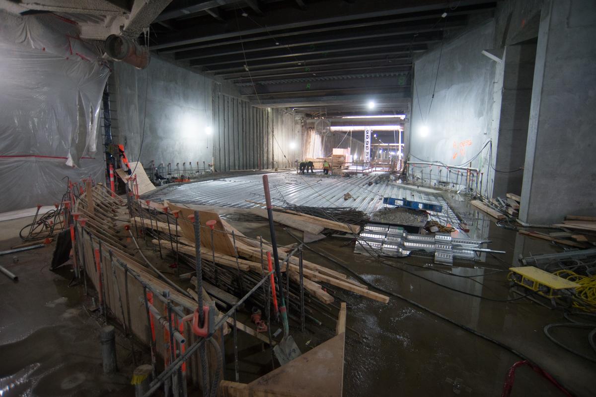Construction site with concrete forms and metal framework under bright lighting in an underground transit tunnel.