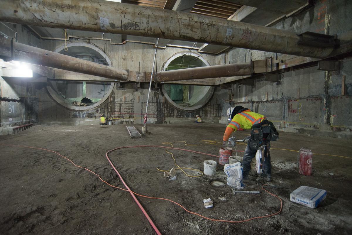 Worker in safety vest mixing cement inside underground transit station under large circular tunnel sections.