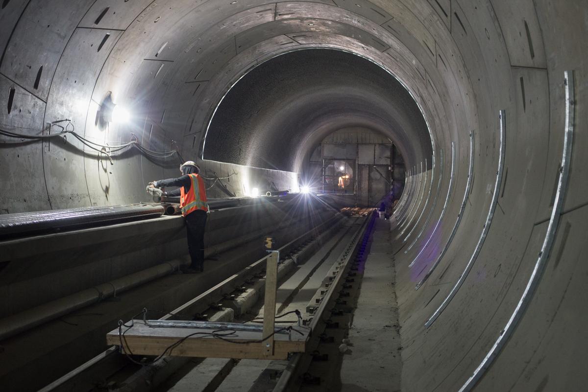 Worker in safety vest installing utility conduit pipe inside concrete transit tunnel under construction.