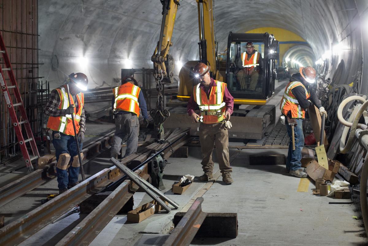 Workers install rail sections in underground tunnel during transit construction project.