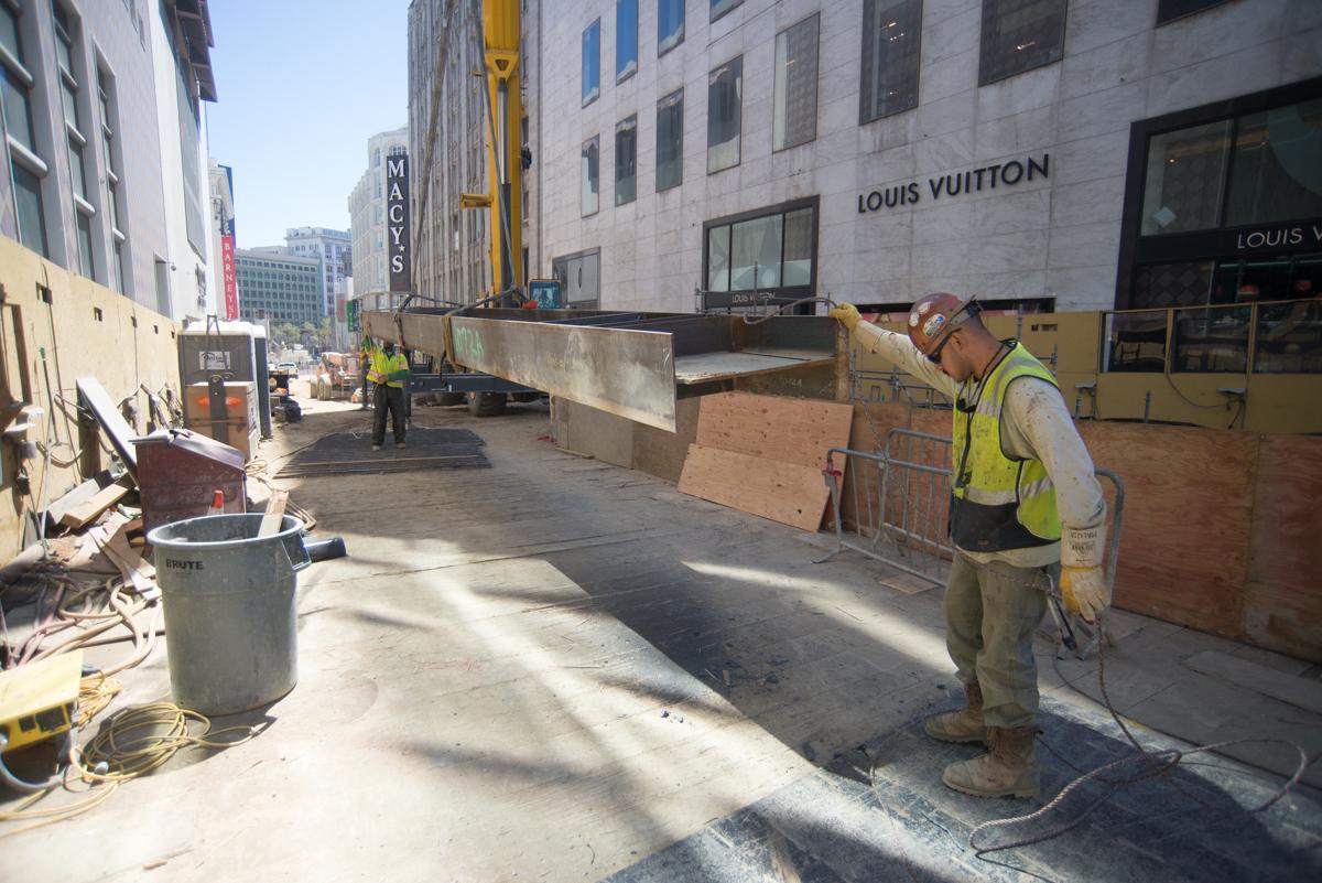 Construction worker operating jackhammer on street near Union Square Station with crane and steel beams visible.