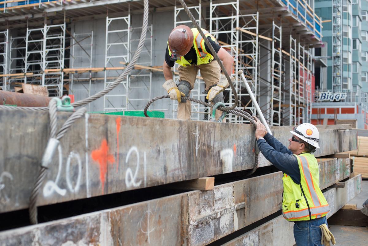 Construction workers installing cables around steel beams at underground transit station site.