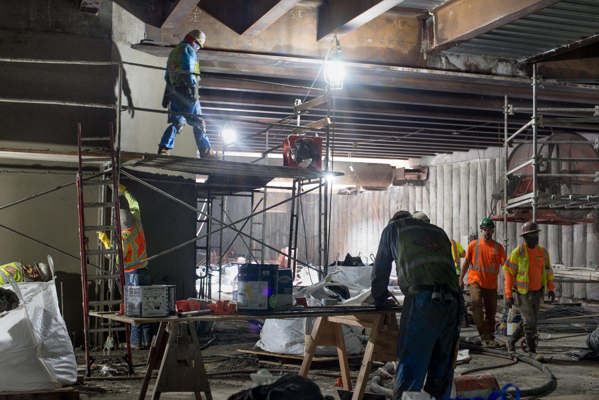 Workers in safety gear construct underground station interior with steel framework and lighting equipment at night.