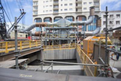 Construction site with excavation pit, ventilation equipment, and ductwork at transit station headhouse.