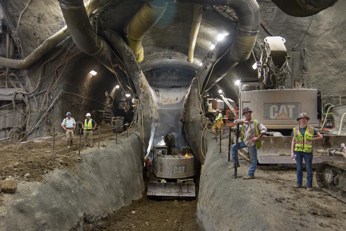 Workers in safety vests observe tunnel excavation and equipment operations at an underground transit construction site.