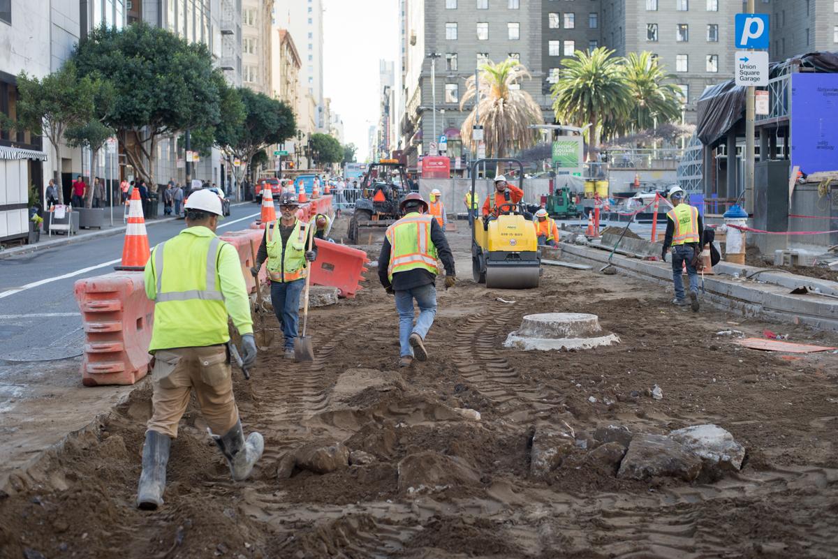 Construction workers in safety vests regrading dirt roadbed on Geary Boulevard near Union Square.