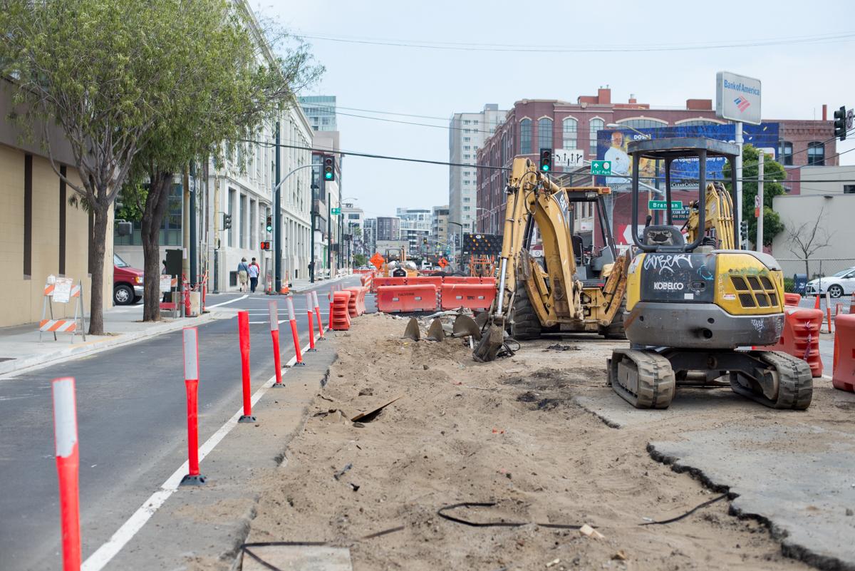 Construction equipment and excavation work on 4th Street with red and white safety barriers lining the street.