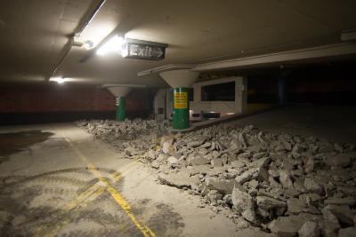 Underground garage interior with concrete debris pile, yellow floor markings, and construction equipment during demolition work.