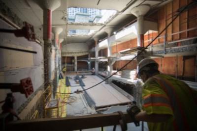 Worker in safety vest inspects equipment on temporary wooden deck inside Union Square garage during demolition.