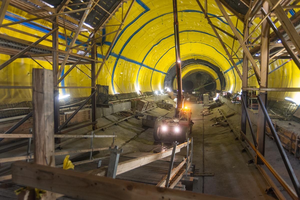 Underground tunnel under construction with yellow support structure and equipment vehicle with headlights