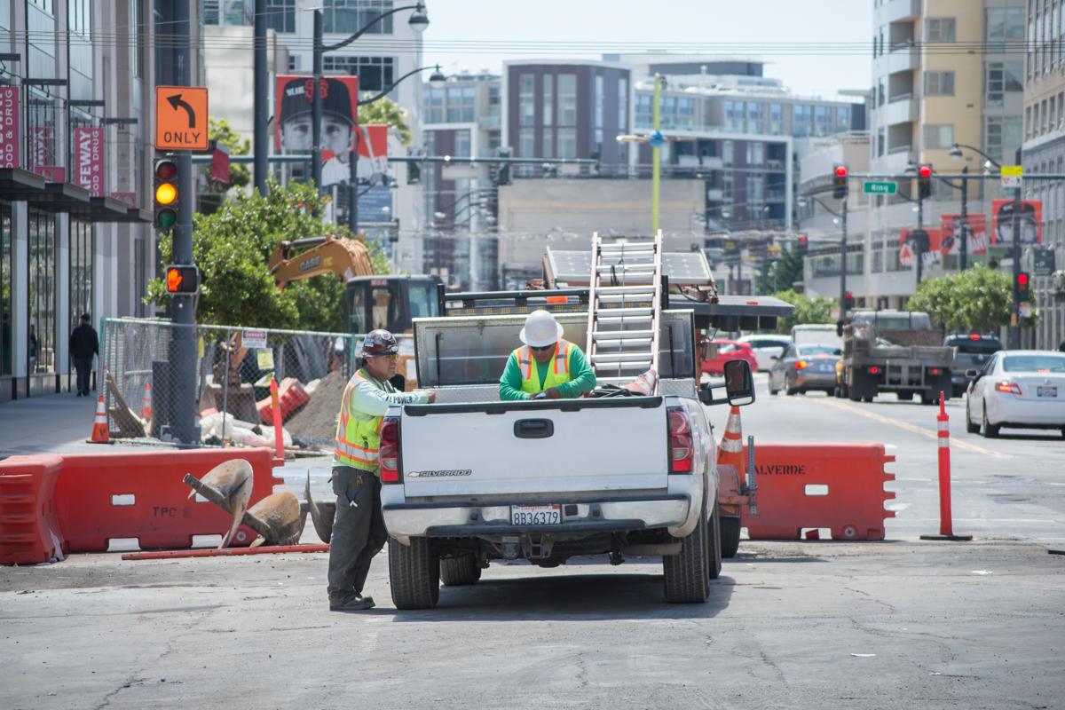 Construction crew working on street utilities at 4th and Townsend intersection with white truck and traffic barriers.